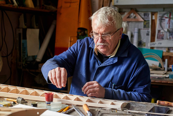 Idősebb ember, aki a műhely asztalán egy rádióvezérlésű repülőgép fából készült szárnyát készíti, a repülőgép megépítését.. - Fotó, kép