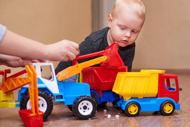 Maman montre à son petit fils comment jouer avec un tracteur à jouets et un camion à benne basculante. - Photo, image