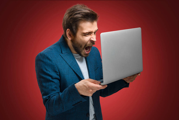 The young man screams in rage. A guy with a beard holds a laptop in his hands. Business failure. Market crash. The trader has lost a lot of money. Stock market flop - Фото, зображення