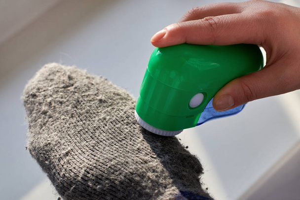 Mulher remove fiapos de meias de lã com a ajuda de uma máquina elétrica, close-up. - Foto, Imagem