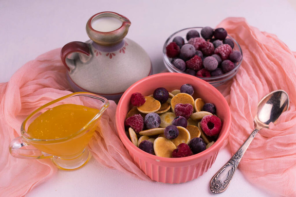Mini crêpes aux baies congelées et miel et une cruche de lait sur la table. Délicieux petit déjeuner concept - Photo, image
