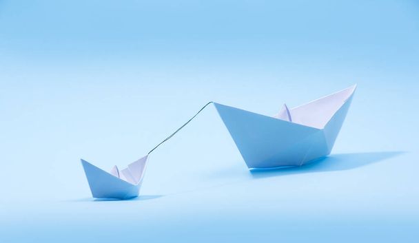 紙のボート-青い背景に大きなボートを引くタグボートやリムーカー。小さなヘルパーコンセプト、タグボート - 写真・画像