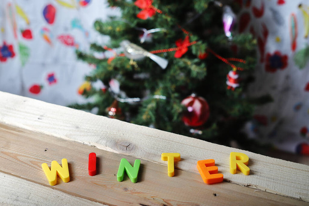 the inscription winter in plastic color letters on the wooden background against the christmas tree - Photo, image