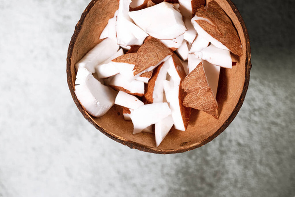 A bowl of coconut pieces on concrete background. Coconut ingredient on plate. Vegan organic snack in zero waste coconut bowl. High quality photo - Foto, Bild