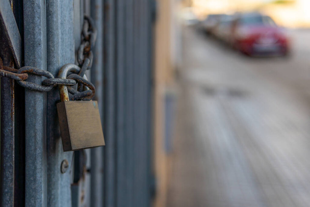 Fence of a closed business with a chain and a lock. In the background an unfocused urban street with bokeh - Photo, Image