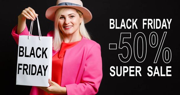 Portrait of smiling woman in straw hat holding packages bags with purchases after shopping with black friday sale written isolated on black background. inscription black friday - Foto, Bild
