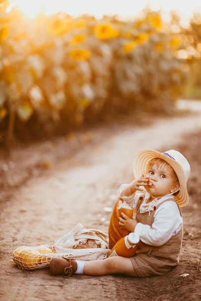 a boy in a field of sunflowers eats wheat bread, the loaf is partially bitten off - Фото, изображение
