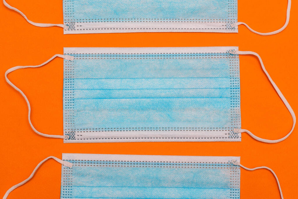 Медицинские маски на оранжевом фоне. Синяя хирургическая маска для защиты от эпидемии ковида-19. Защищает рот и нос от бактерий и вирусов. Дыхательная защита, медикаменты. - Фото, изображение