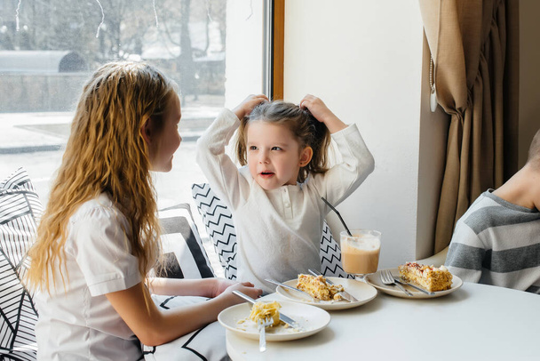 Two cute little girls are sitting in a cafe and playing on a Sunny day. Recreation and lifestyle. - Фото, изображение