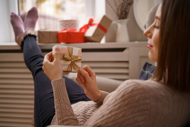Женщина сидит в кресле дома с подарком в руке - Фото, изображение