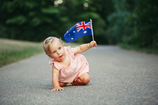 Schattig schattig blank meisje zwaaiend met Australische vlag. Grappig kind kruipt op straat in het park vieren Australië Dag vakantie. Viering van de nationale Australië Dag in januari outdoor. - Foto, afbeelding