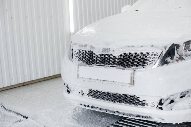 Modern washing with foam and high-pressure water of a white car. Car wash - Zdjęcie, obraz