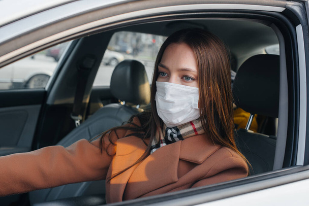 Nuori tyttö istuu ratissa autossa naamiossa maailmanlaajuisen pandemian ja koronaviruksen aikana. Karanteeni - Valokuva, kuva