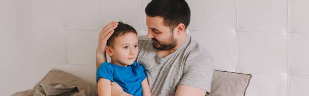 Caucasian father talking to boy son. Man parent hugs kid child on bed in bedroom at home. Authentic lifestyle real family candid moment. Happy Fathers Day holiday. Serious talk. Web banner header. - Photo, Image