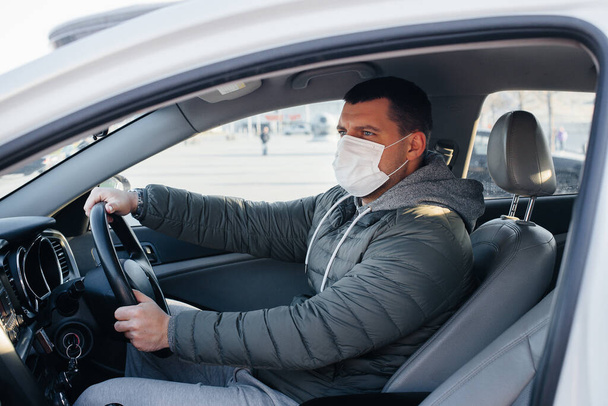 A young man sits behind the wheel wearing a mask for personal safety while driving during a pandemic and coronavirus. Epidemic - Foto, immagini