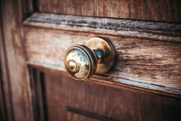 Egy régi, nosztalgikus fém ajtógomb egy sötét fából készült ajtón, amelynek a felülete már enyhén korrodált és kopott, és az ajtó közepére van erősítve.. - Fotó, kép