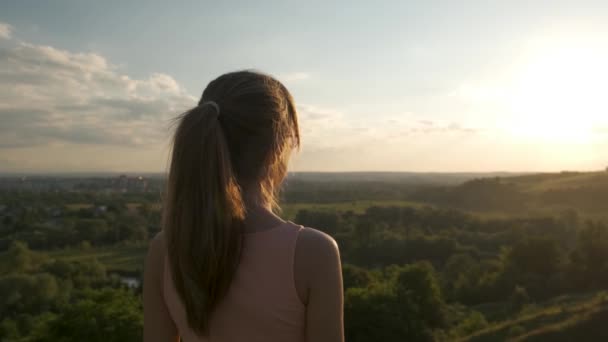 Fiatal nő áll a zöld területen élvezi naplemente kilátás az esti természet. Relaxációs és meditációs koncepció. - Felvétel, videó