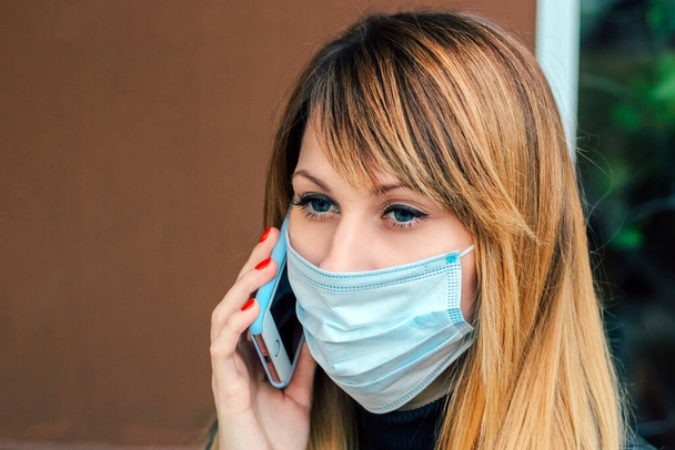 blonde girl with red manicure talking on the phone. Girl in medical mask. - Photo, Image