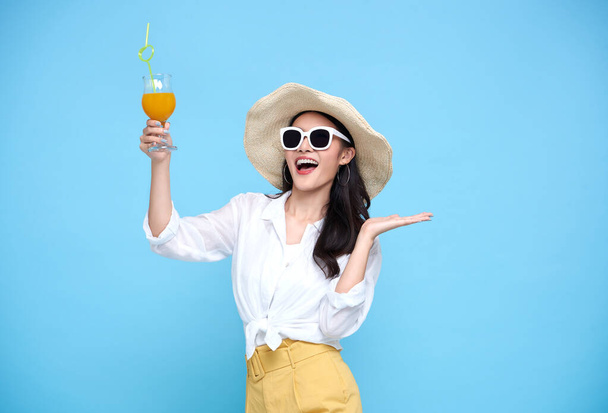 Šťastná asijská žena v létě ležérní oblečení nosí slaměný klobouk, sluneční brýle drží sklenici čerstvé ovocné šťávy nápoj izolované na jasně modrém pozadí. - Fotografie, Obrázek