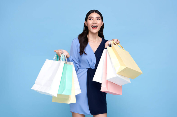 Happy kaunis Aasian shopaholic naiset yllään sininen mekko ja tilalla ostoskassit eristetty sinisellä pohjalla. - Valokuva, kuva