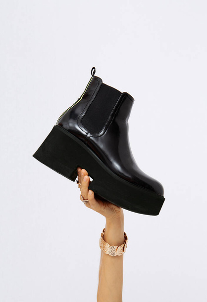 Hand in the studio holds  platform boots. Trendy  shoes.  Minimalist fashion style concept - Photo, Image