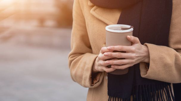 Close up on womans hands holding a cup of coffee wearing beige coat on the street female fashion. Portrait of stylish young woman wearing autumn coat and red beret outdoors. Autumn accessories - Fotó, kép