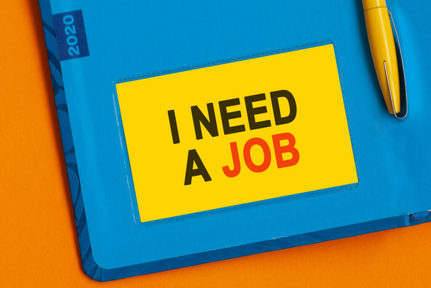 Les mots "J'ai besoin d'un emploi" sont écrits en lettres noires sur papier jaune. Un stylo jaune est intégré dans le fond du journal bleu. - Photo, image