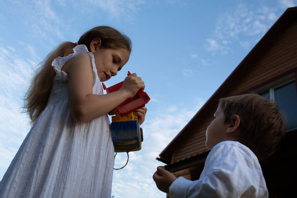 A girl is repairing a toy for little boy. Children stand against the blue sky. - Foto, Bild