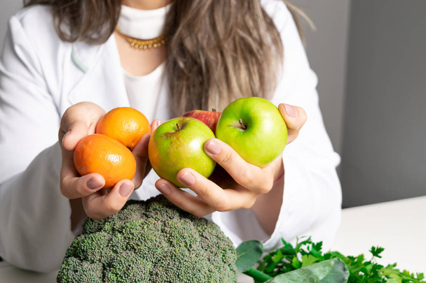 Női táplálkozási szakértő az irodájában, egészséges zöldségeket és gyümölcsöket mutat. Egészségügyi és diéta koncepció. Életmód. - Fotó, kép