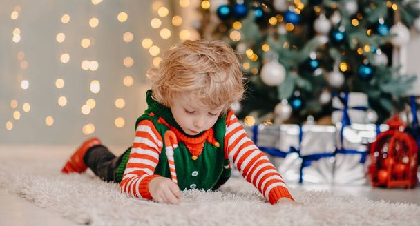 Petit garçon rêveur écrivant une lettre au Père Noël couché sur le sol dans une pièce décorée, attendant des cadeaux et un miracle - Photo, image