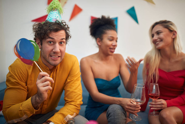bored caucasian guy in company of two multiethnic females making funny face at the party. looking at camera, eye contact - Foto, imagen