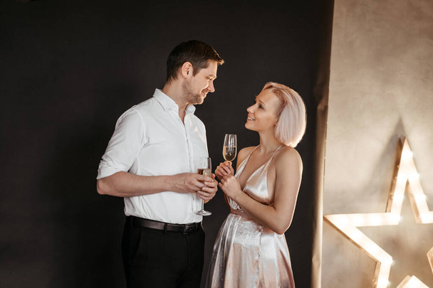 Beautiful happy couple young family in evening dresses with glasses of champagne on the dark background, selective focus - Foto, Imagen