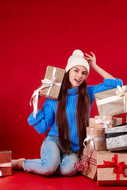 girl in a knitted hat with New Years gifts on a red background - Photo, Image
