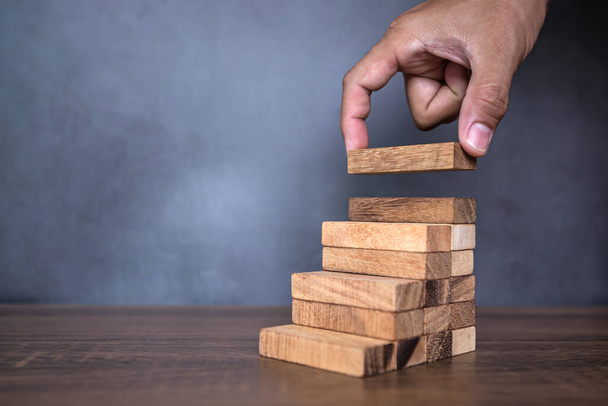Close-up hand is placing wood block tower stacked in pyramid shape with caution to prevent collapse or crash concepts of financial risk management and strategic planning. - Photo, Image
