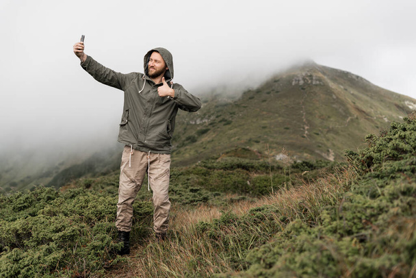 Jeune voyageur se tient sur le sommet de la montagne et prend une photo sur un smartphone par derrière. Endroit pour le texte. Concept de tourisme. - Photo, image