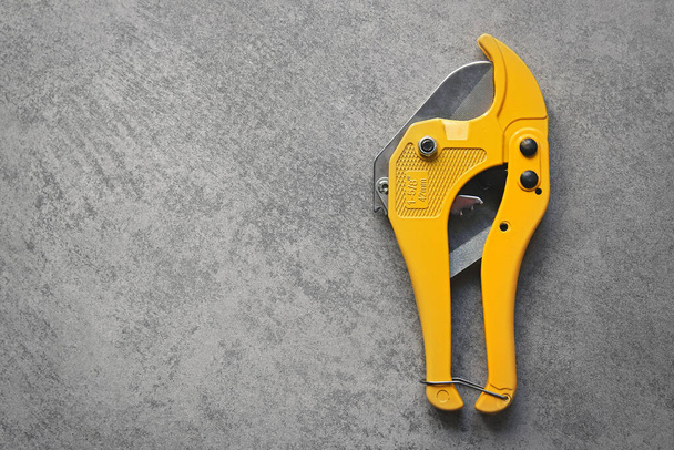Yellow scissors for cutting pvc plastic pipes on grey background with copy space - Valokuva, kuva