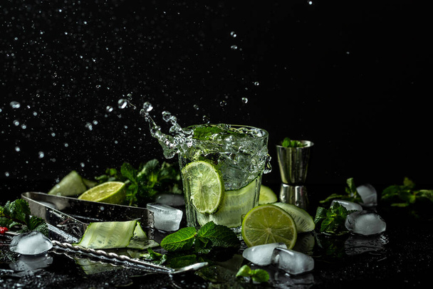 Summer homemade lemonade made from lime, lemon, cucumber with ice in glass, drink with liquid splash, freeze motion in jar glass on dark background. - Photo, Image