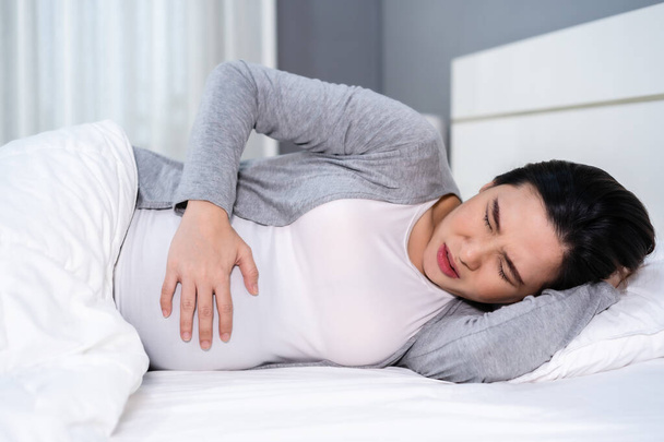 pregnant woman has a stomachache on a bed - Фото, изображение