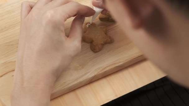 Close up of Chef picking up and squeezing sugar cream on Christmas homemade gingerbread man cookies on wooden tray - Footage, Video