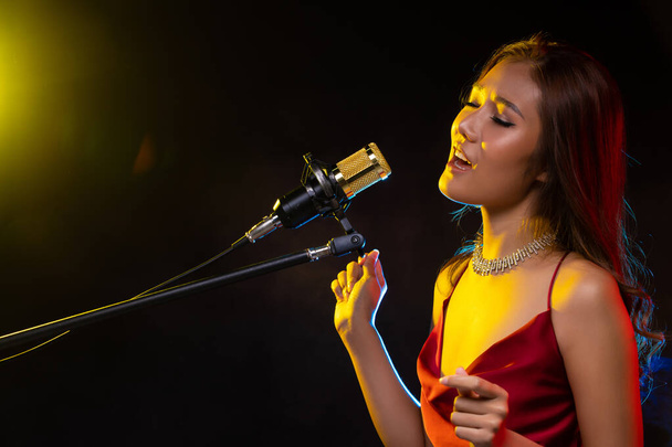 Asian Woman bruin krullen haar dragen rode jurk zingen een lied luid macht geluid over opknoping microfoon condensor, componist. Absorberende rookruimte, kopieerruimte - Foto, afbeelding