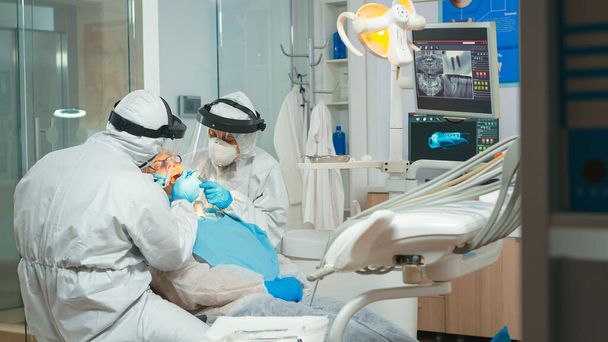 Stomatolog v ochranném obleku provádí zubní prohlídku - Fotografie, Obrázek