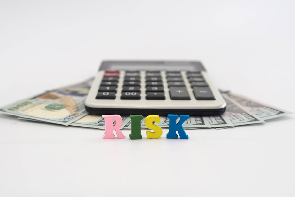 Dollars, rekenmachine en het woord "risico" gelegd uit gekleurde letters op een witte achtergrond. Het concept van de economische crisis, bedrijfsrisico. - Foto, afbeelding