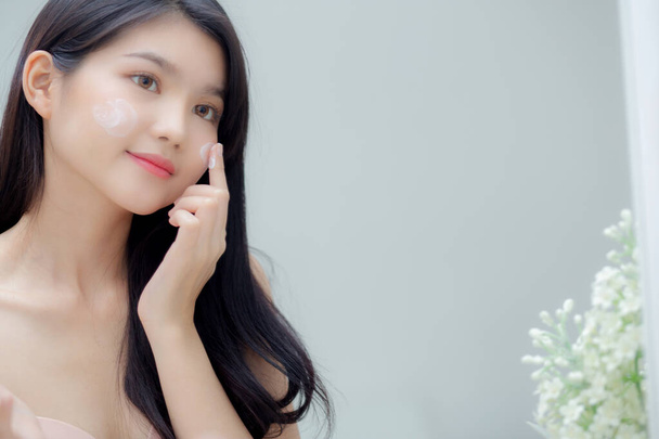 Hermosa joven asiática mujer sonriente mirada en el espejo de comprobar la cara con el cuidado de la piel y cosmética para el rejuvenecimiento y la higiene, belleza chica feliz facial limpio con crema o loción y para la salud. - Foto, Imagen