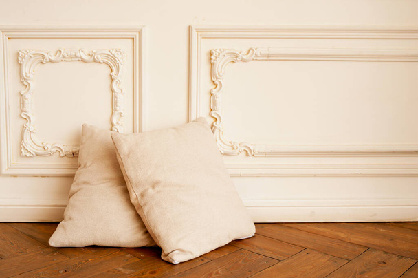 dos almohadas beige suaves y acogedoras en el suelo de parquet de madera y contra la pared de moldeo de estuco blanco. minimalismo en el interior, enfoque selectivo - Foto, imagen