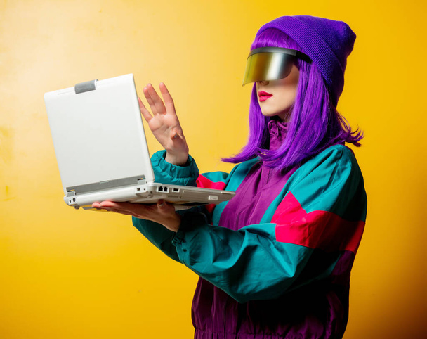 Style woman in VR glasses and 80s tracksuit with laptop on yellow background - Foto, immagini