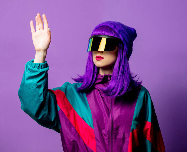 Stylistin mit VR-Brille und 80er-Jahre-Trainingsanzug auf violettem Hintergrund - Foto, Bild