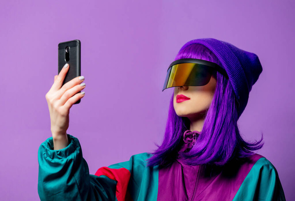 Style femme en lunettes VR et survêtement 80 's avec téléphone portable sur fond violet - Photo, image