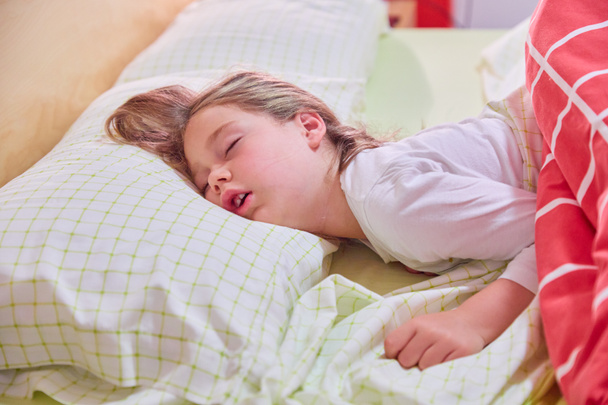 Sarışın, beyaz, beş yaşında ağzı açık ve yüzünde komik bir ifadeyle kral yatağında uyuyan bir kız. - Fotoğraf, Görsel