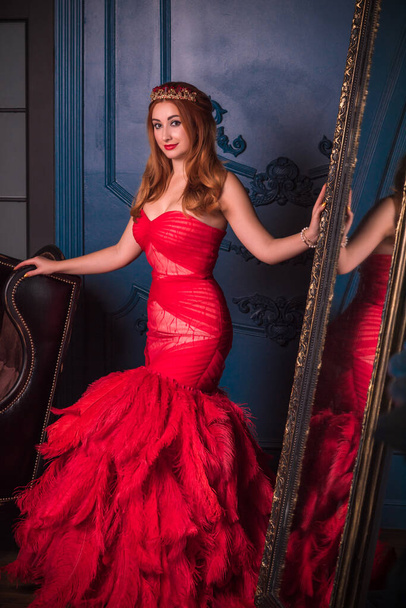 Frau im wunderschönen roten Abendkleid. Ziemlich nette Dame an Heiligabend. Frau in schönem Kleid mit Federn  - Foto, Bild