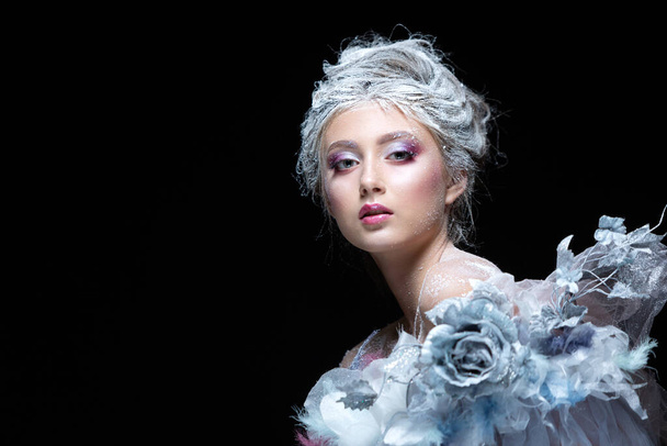 Winter Beauty Woman in clothes made of frozen flowers covered with frost, with snow on her face and shoulders. Christmas Girl Makeup. Make-up the snow Queen. Isolated on a black background. - Foto, Imagen